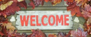 Colorful fall leaves border red wooden welcome sign with wood hearts